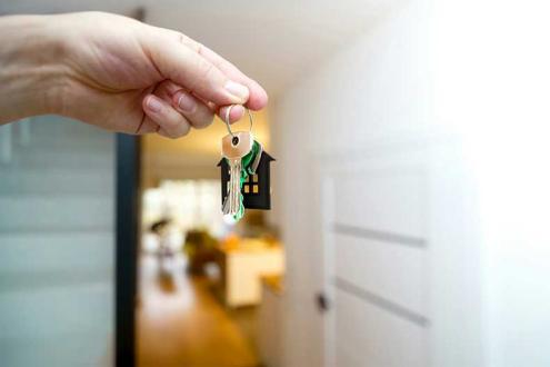 A close-up of a hand holding a set of house keys with a small house-shaped keychain, symbolizing new homeownership