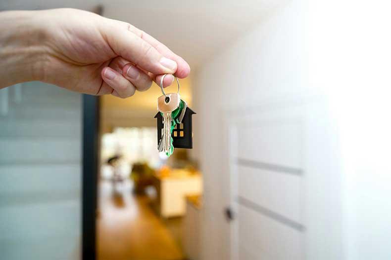 A close-up of a hand holding a set of house keys with a small house-shaped keychain, symbolizing new homeownership